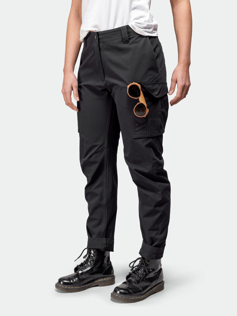 Person som bär Halti Roams Cargobyxor Dam, vit t-shirt, svarta stövlar och bruna solglasögon fasthakade i en ficka.