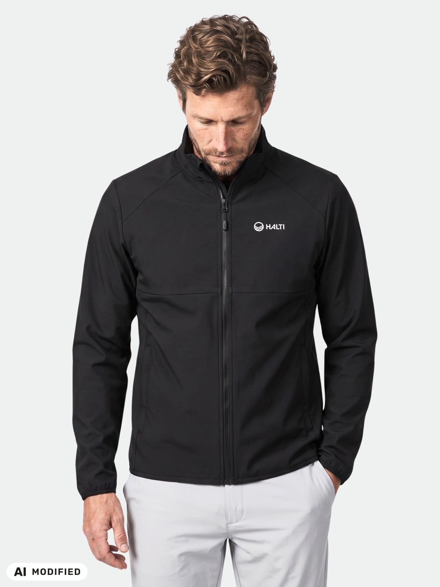 En man bär en Halti Wedge Softshell Jacka Herr, perfekt för friluftsliv, mot en ljus bakgrund.