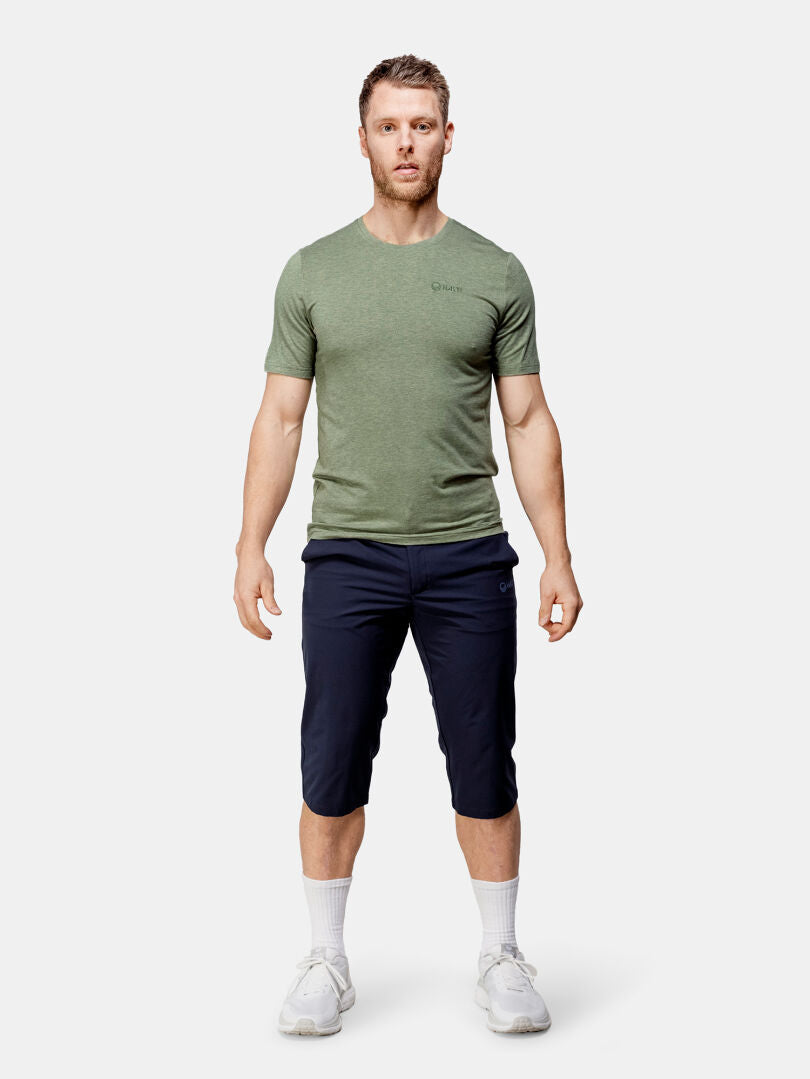 En man bär en grön t-shirt, Halti Drive X-stretch Capribyxor Herr UPF 50+, vita strumpor och vita sneakers.