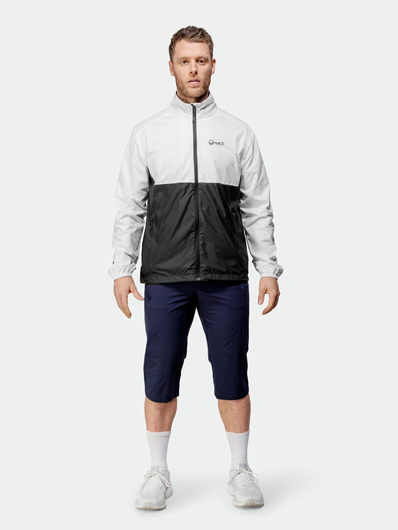 En man vetter framåt i en Halti Saime Vindjacka Herr-jacka, marinblå shorts, vita strumpor och vita sneakers.