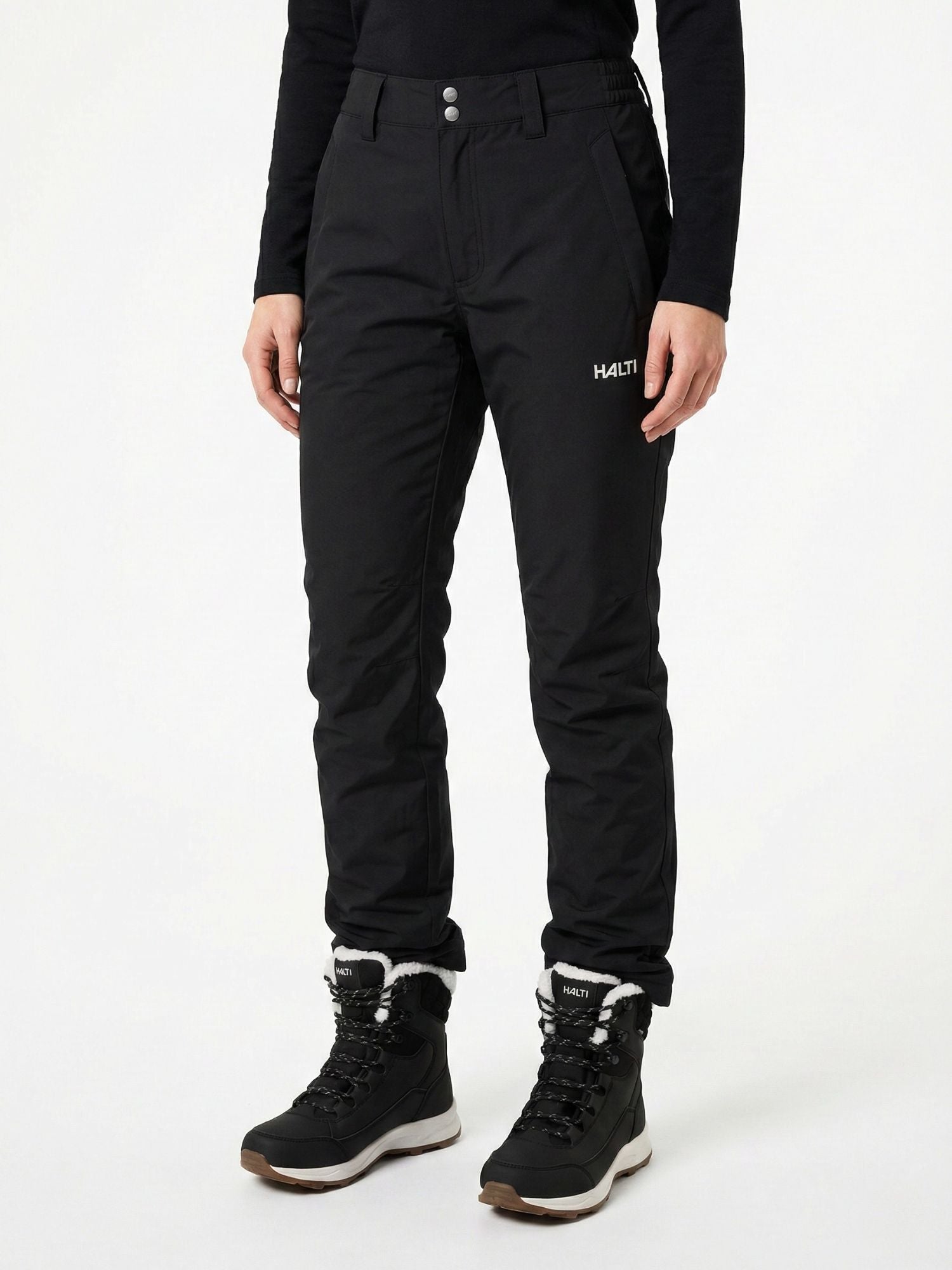 Person iklädd Halti Routa Vinterbyxor Dam och svarta stövlar med vit kant, stående mot en vit bakgrund.