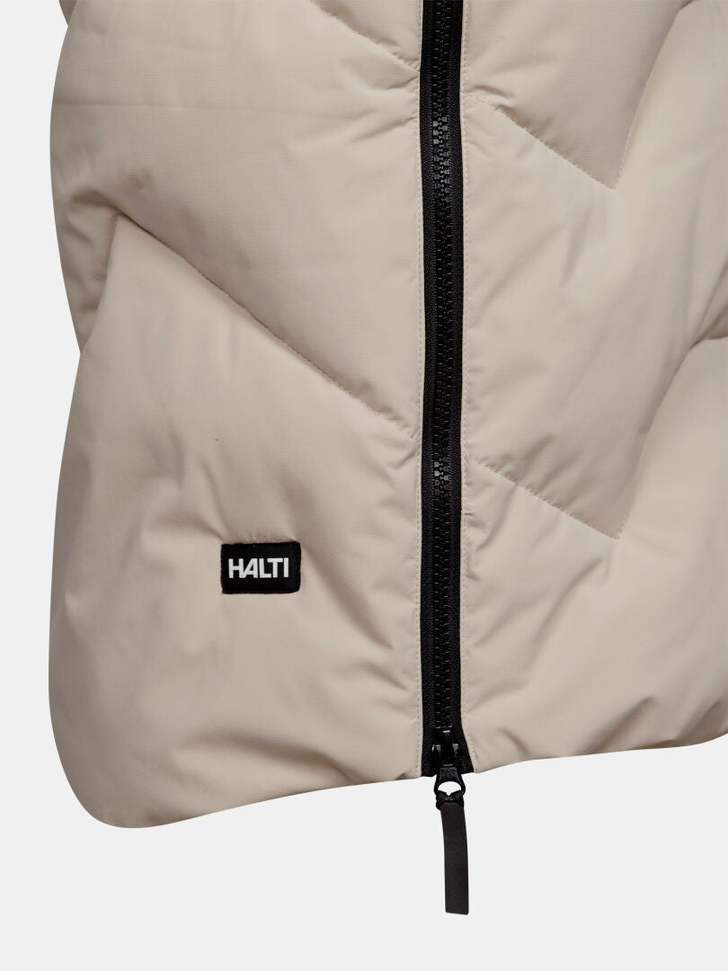 Närbild på Halti Brahe Puffer Long vinterjacka för dam i beige med svart dragkedja och en liten svart applikation vid sömmen.