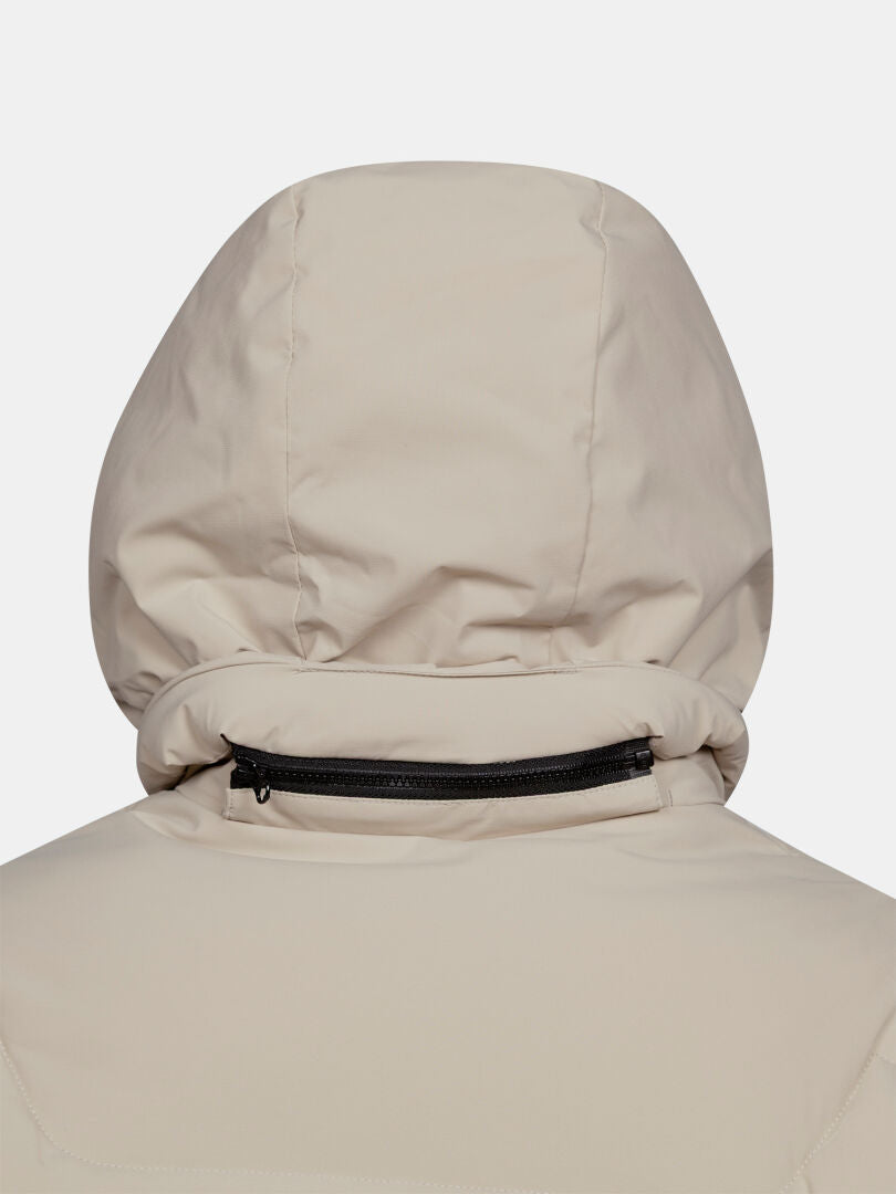 Närbild på baksidan av en beige Halti Brahe Puffer Long Vinterjacka för dam med en svart dragkedja på huvan.