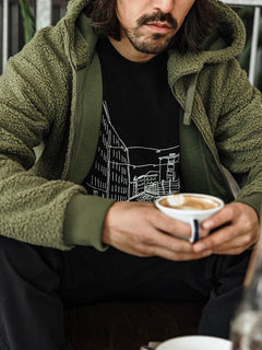 Iförd en Halti Lykky Fleecejacka Herr håller en person i en latte art coffee och kopplar av inomhus.