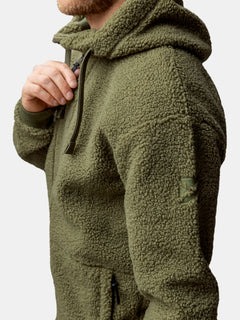 En person bär Halti Lykky Fleecejacka Herr, en olivgrön huvtröja i återvunnen polyester med dragkedja och uppdragen huva.