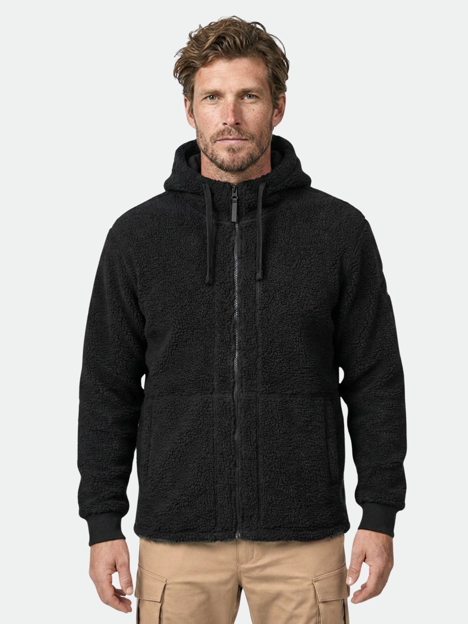 En man i svart Halti Lykky Fleecejacka Herr och beige cargobyxor står mot en enfärgad bakgrund.