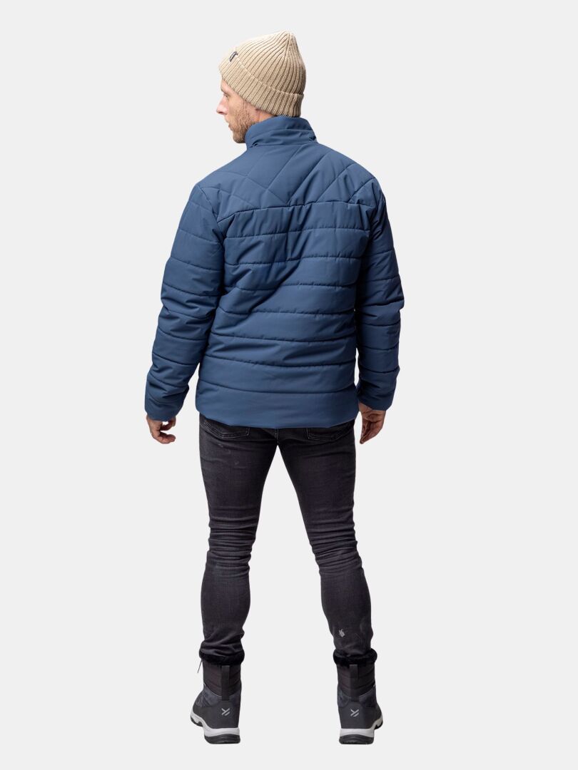 En man i Halti Haapa Vadderad Jacka Herr, svarta jeans, kängor och beige mössa står vänd bort.