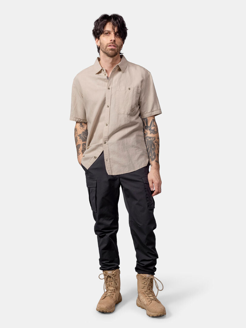 Man mot en enfärgad bakgrund iklädd en beige Halti Notsgi Skjorta Herr, svarta byxor och solbruna stövlar.