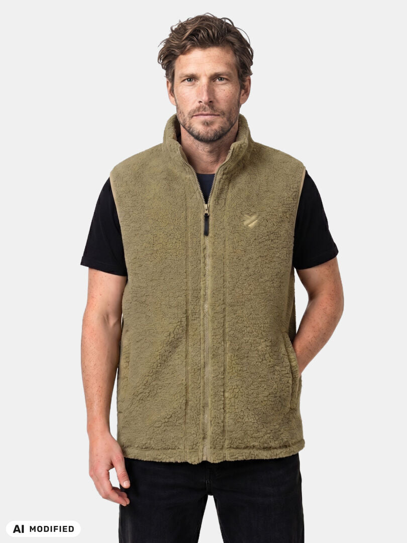 Man i Halti Lykky Fleece Väst Unisex (beige, återvunnen polyester) över en svart T-shirt, mot en ljus bakgrund.