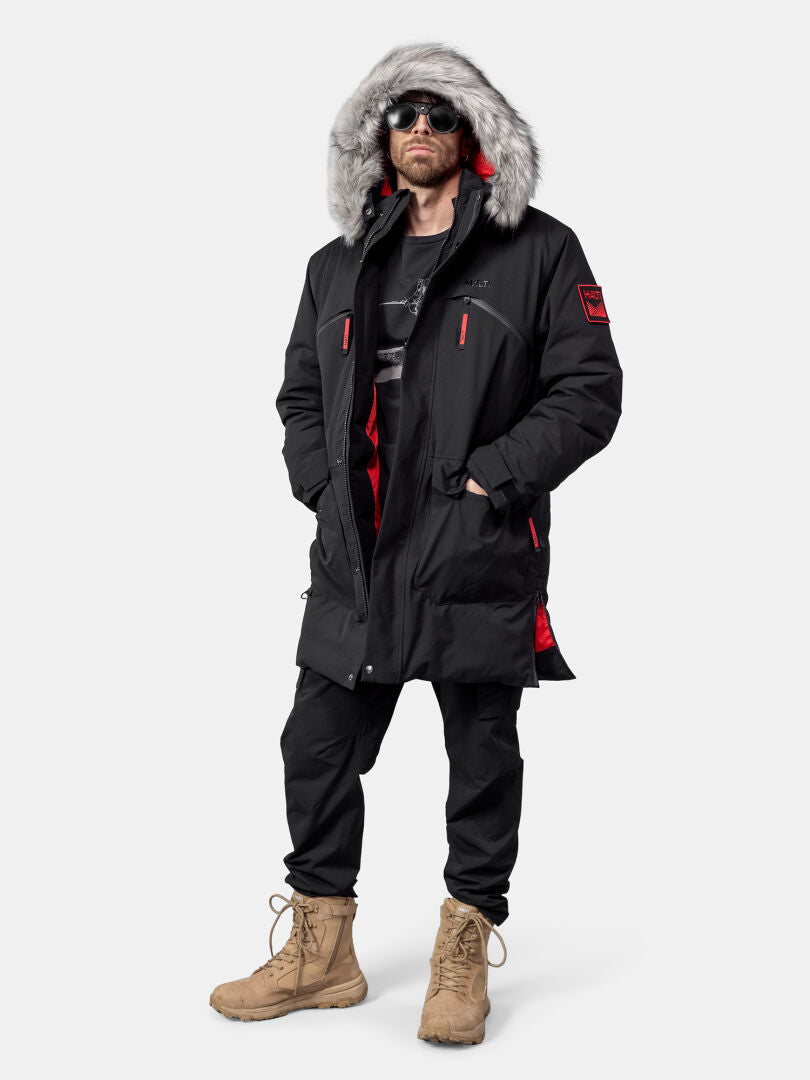 Man i Halti 1976 Down Parka Unisex by Halti, med pälskantad huva, svarta byxor, solbruna stövlar och solglasögon, stående upprätt.