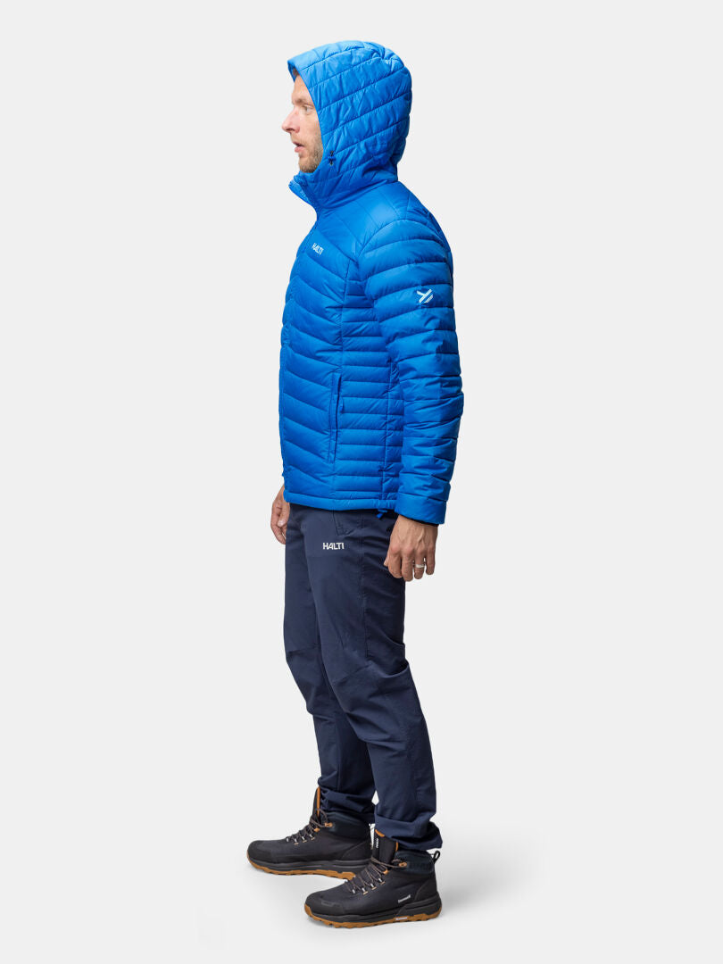 En man i en Halti Huippu Dunjacka Herr med Pertex Quantum står i profil mot en enkel bakgrund.