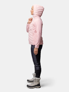Person i Halti Huippu Hybrid Dunjacka Dam (rosa), svarta byxor och grå stövlar mot en enfärgad bakgrund.