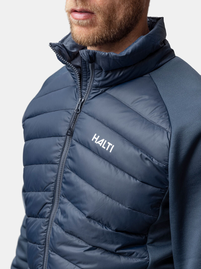 En man bär Haltis Huippu Hybrid Dunjacka Herr i blått med RDS-certifierat dun och Pertex Quantum-tyg.