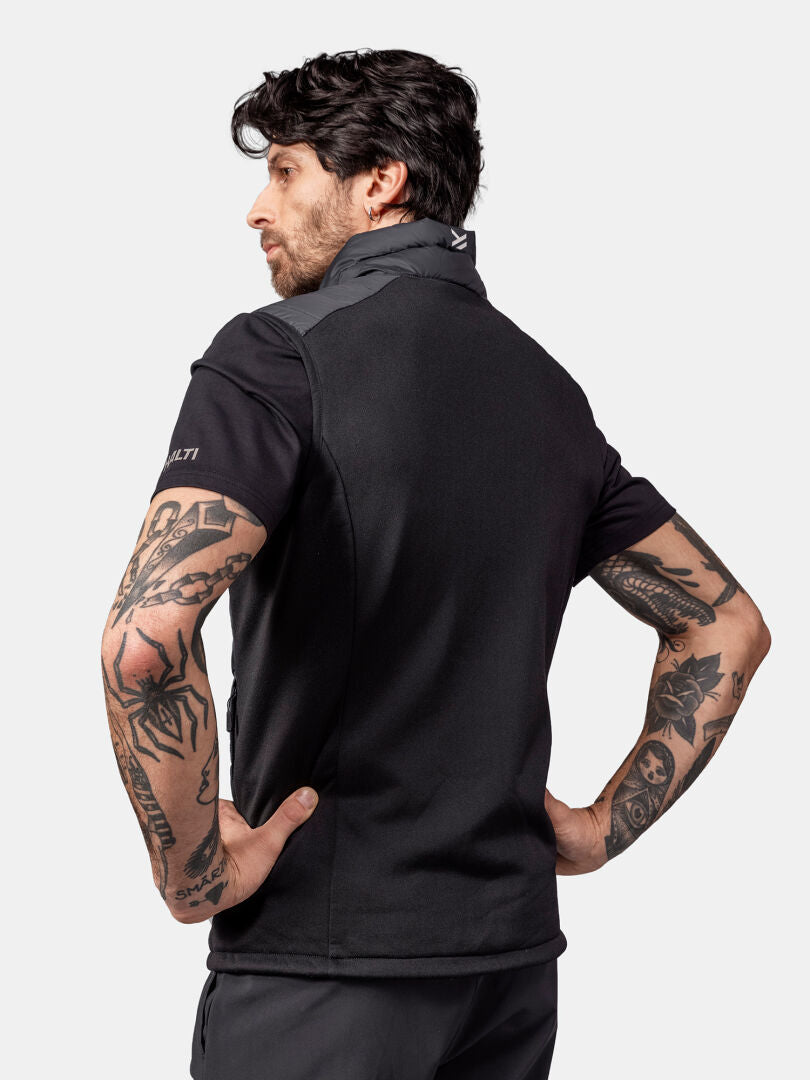 En man i Halti Huippu Dunväst Herr med tatuerade armar står med händerna på höfterna, vänd bort från kameran.