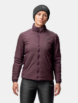 En person bär en rödbrun Halti Haave Insulation Primaloft Jacka Dam, mörk mössa och svarta byxor mot en enfärgad bakgrund.