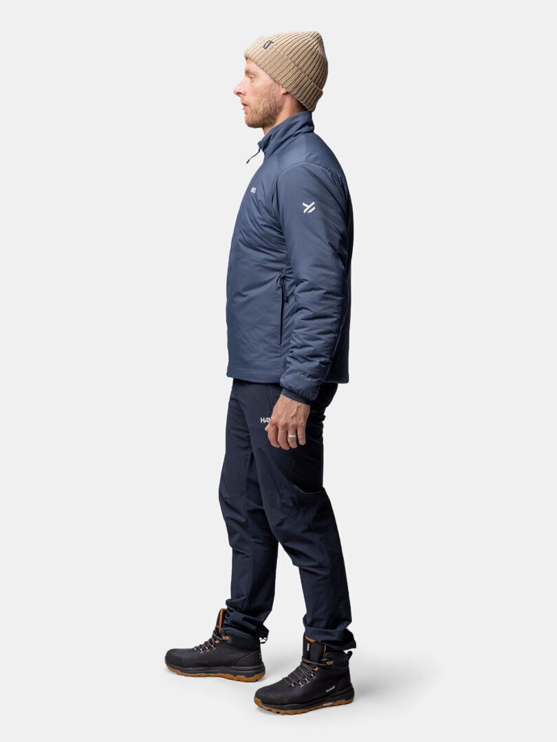 En man i profil bär en blå Halti Haave Insulation Primaloft Jacka Herr, mörka byxor, svarta stövlar och en beige stickad mössa.