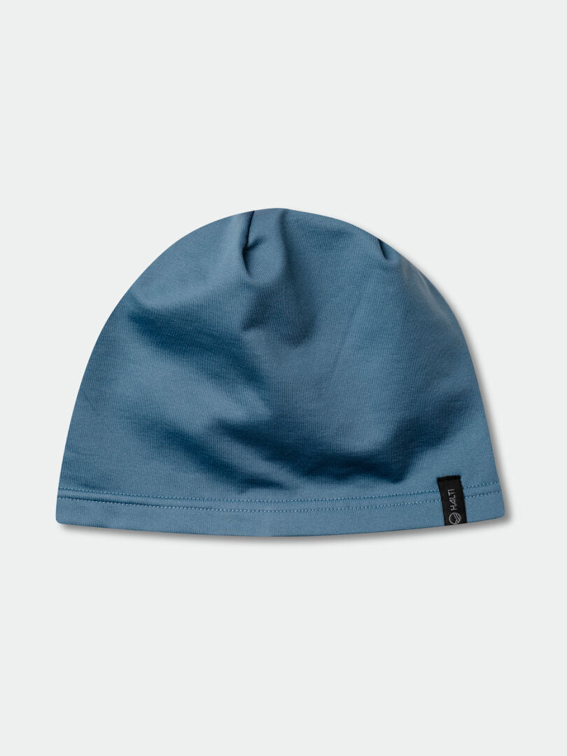 En enfärgad blå Loiva Mössa från Halti, tillverkad av återvunnen polyester, med en liten svart etikett på en ljusgrå bakgrund.