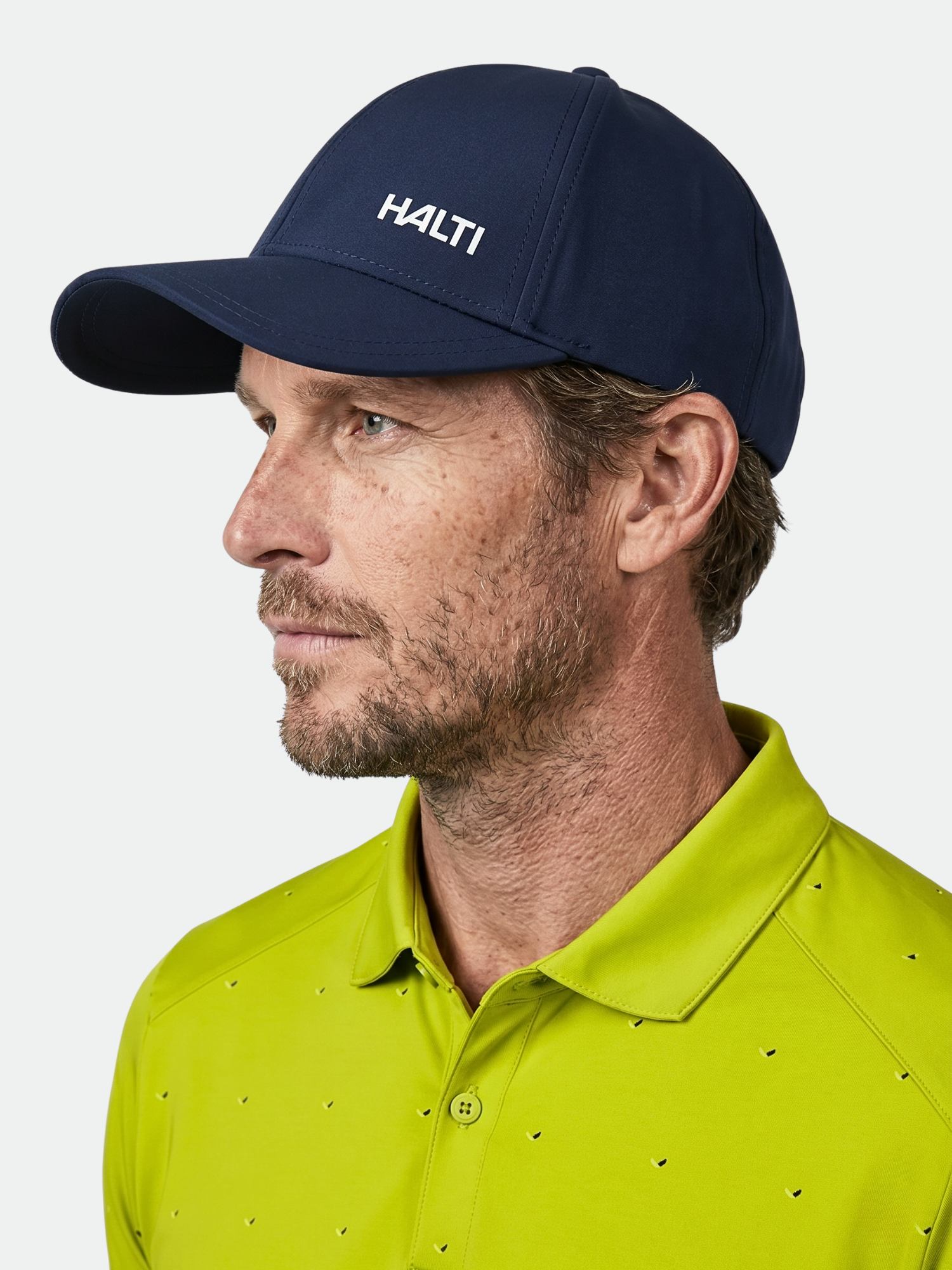 Man med lätt skäggstubb i marinblå Halti Mattas Baseball Keps och ljusgrön polo, sedd från sidan.
