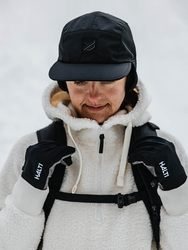 Person med Halti Skutta Keps, Halti-handskar och vit fleecejacka som står ute i snön.