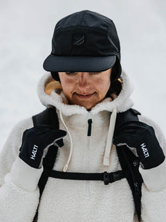 Person med Halti Skutta Keps, Halti-handskar och vit fleecejacka som står ute i snön.