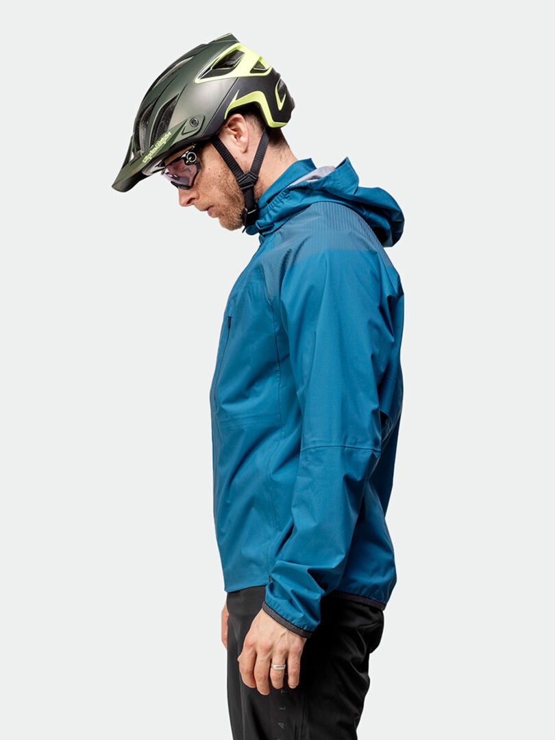 En man i en Halti Liike Herr 3L DrymaxX Sport Jacka, cykelhjälm och solglasögon står i profil mot en enkel bakgrund.