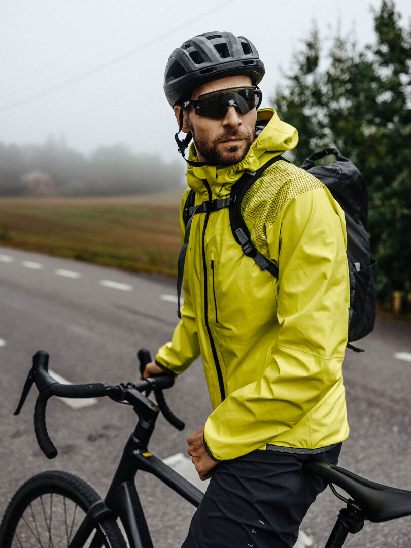 En man i en Halti Liike Herr 3L DrymaxX Sport Jacka och hjälm står med sin cykel på en dimmig väg.