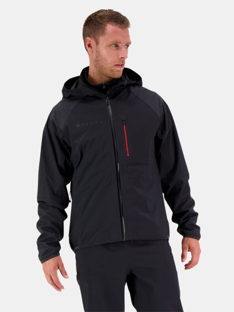 En man bär Halti Liike Herr 3L DrymaxX Sport Jacka, svart med en röd dragkedjaficka, mot en enfärgad ljus bakgrund.