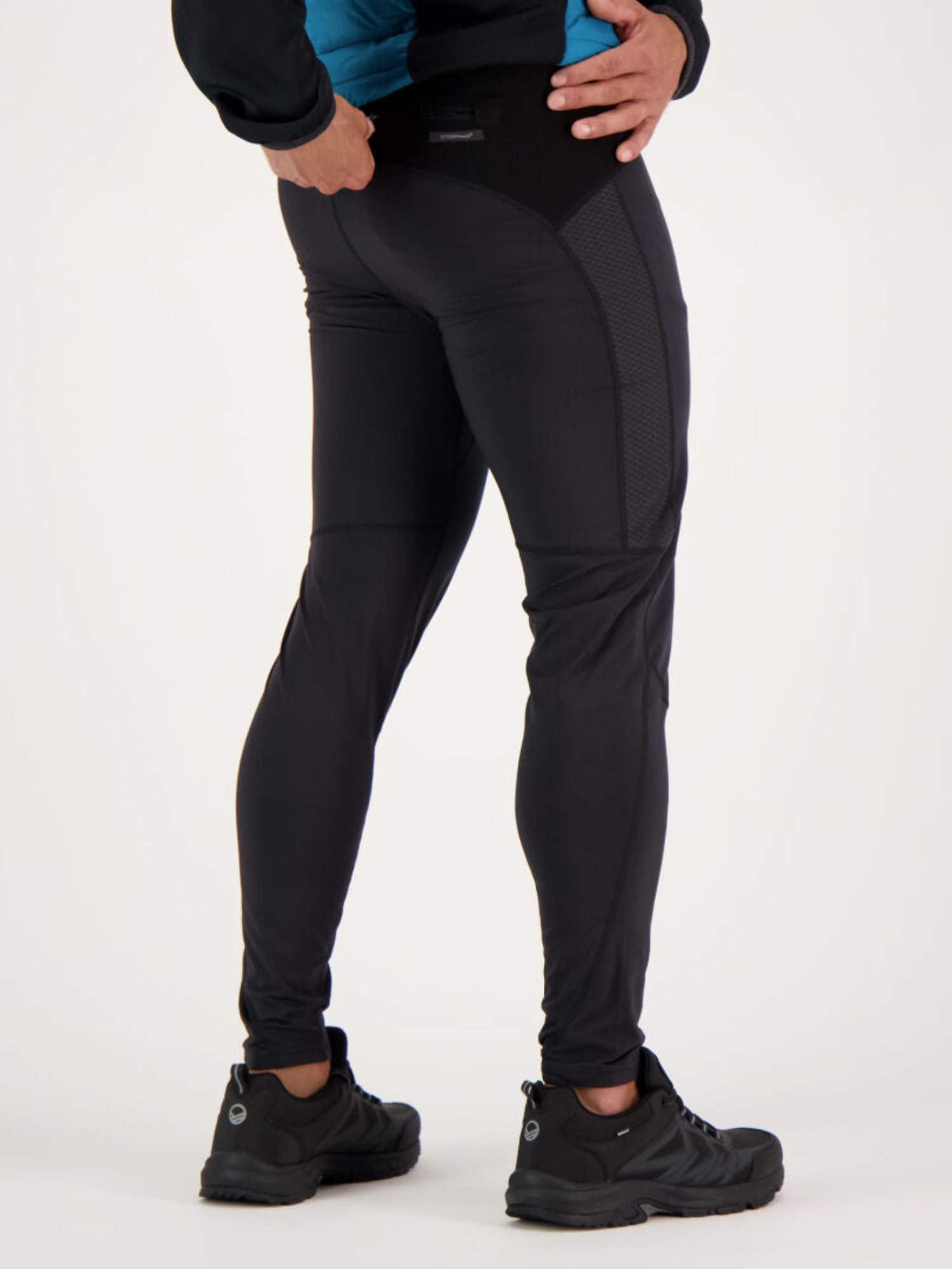 Person iklädd Halti Suunta Herr Hybridtights och svarta sneakers, fotograferad bakifrån mot en ljus bakgrund.