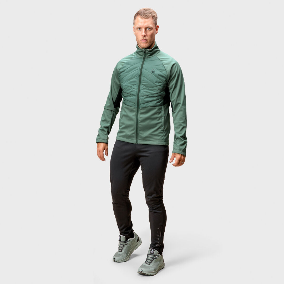 En man står i en Halti Vinha Hybrid Längdskidjacka Herr, svarta byxor och gröna sneakers.