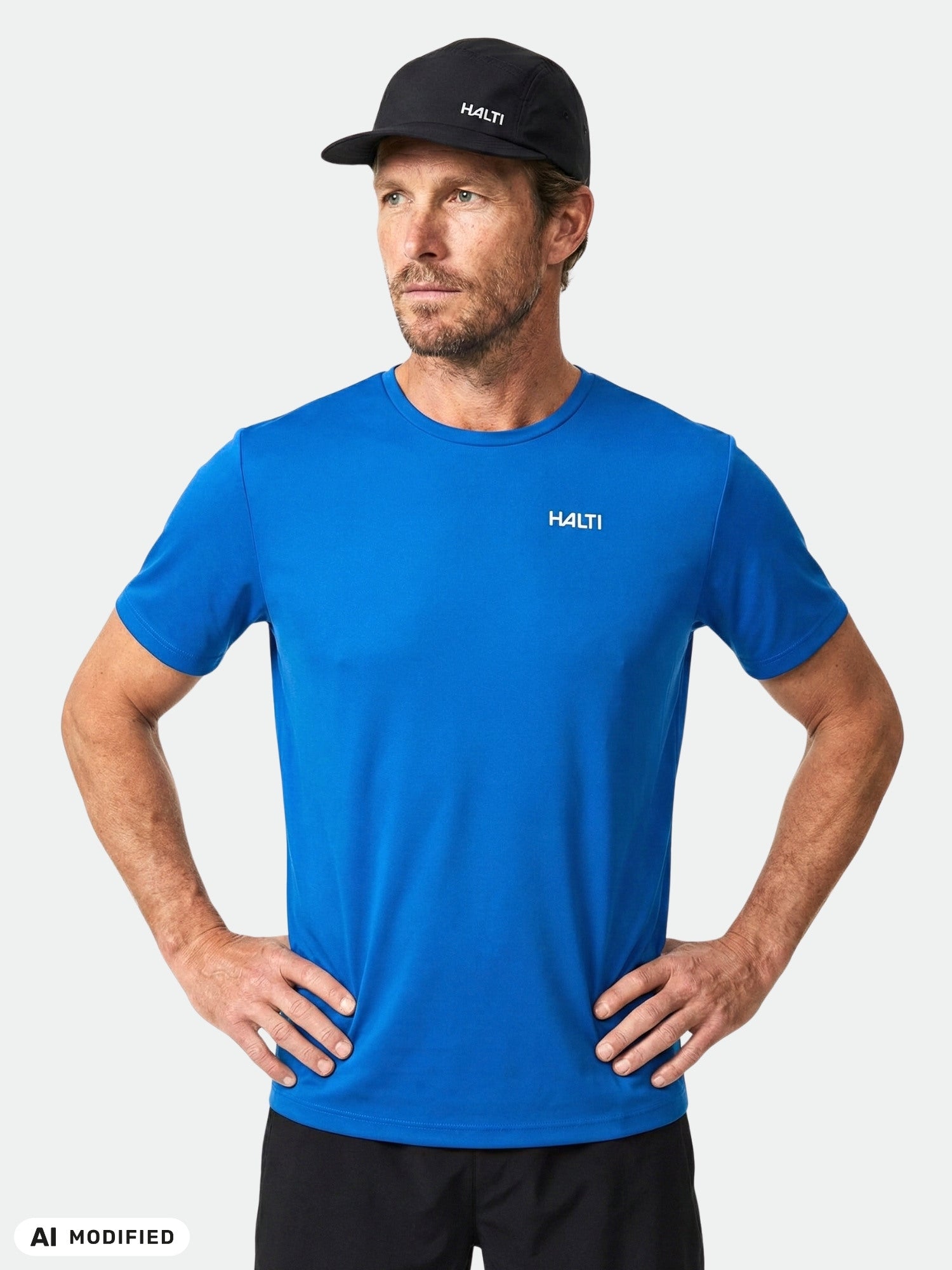 En man i en T-shirt från Halti Salves för herrar, tillverkad av återvunnen polyester, och en svart keps står med händerna på höfterna.