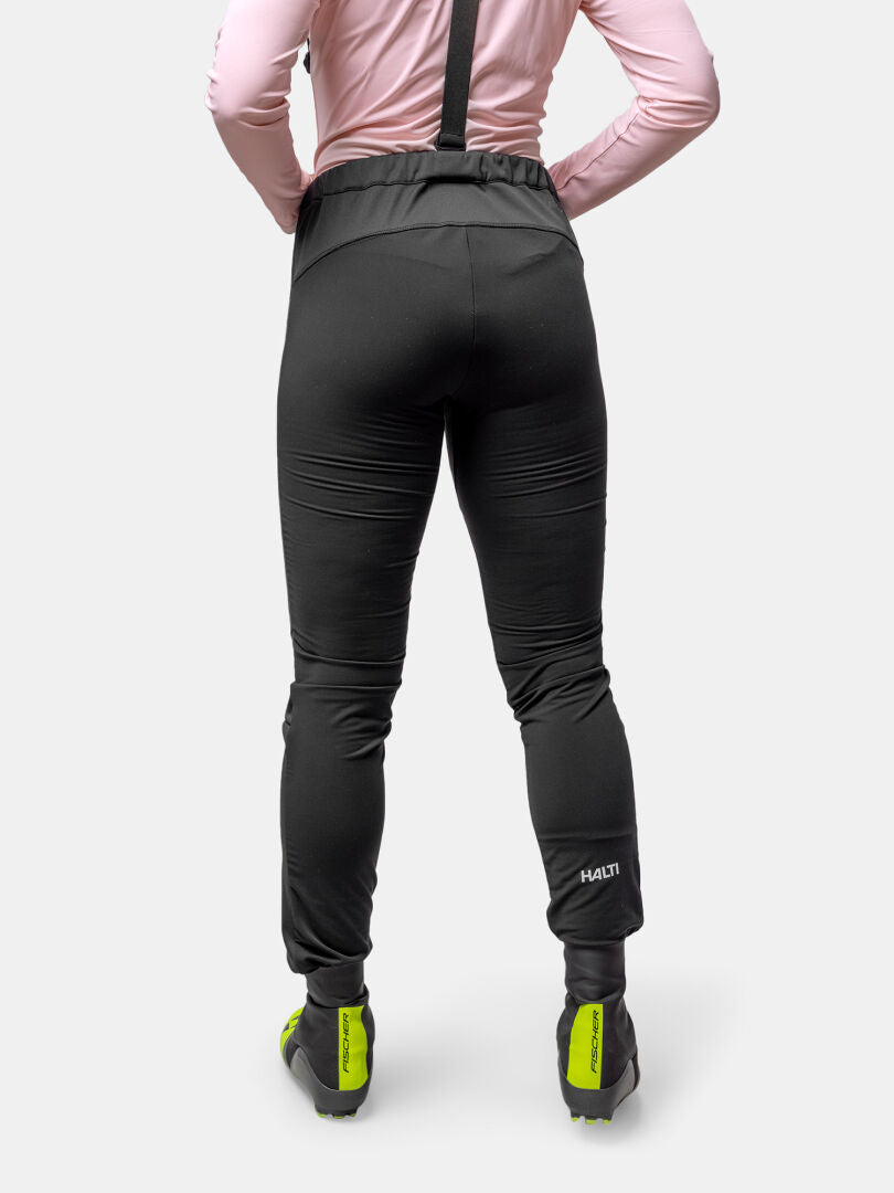 Person i Halti Huuru Längdskiddräkt Dam, rosa topp och neongröna cykelskor - perfekt för vinterträning.