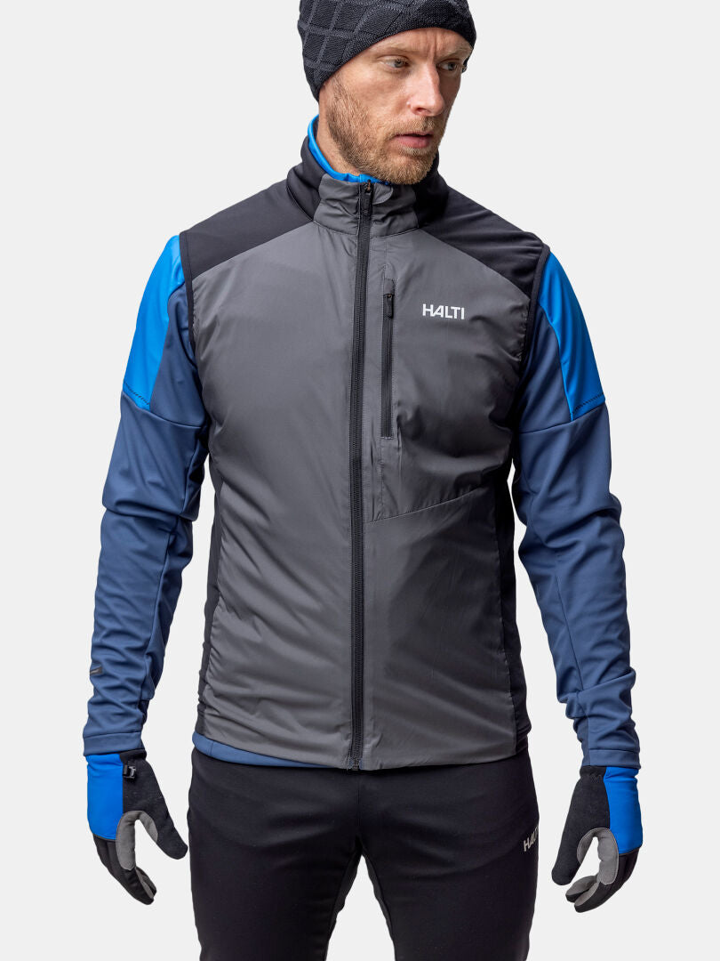 Person iklädd gråblå Halti Framover XCT Väst Unisex, svarta handskar, byxor och stickad mössa, vänd mot höger.