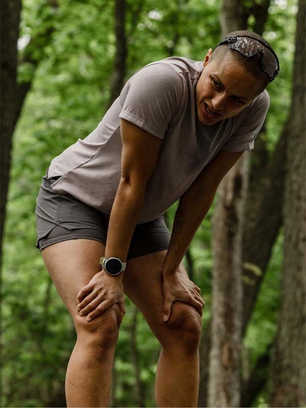 Person i Halti Oulanka T-skjorta Dam (UPF 50+), lutar sig trött framåt i en skogsmiljö.
