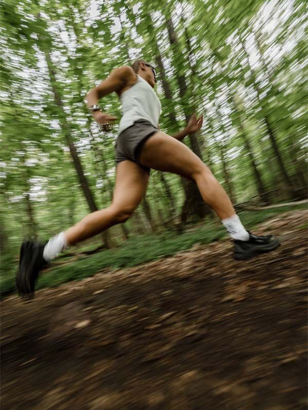 Kvinna springer på en skogsstig i Halti Oulanka T-skjorta Dam med Active Dry och UPF 50+, sett från en låg vinkel.