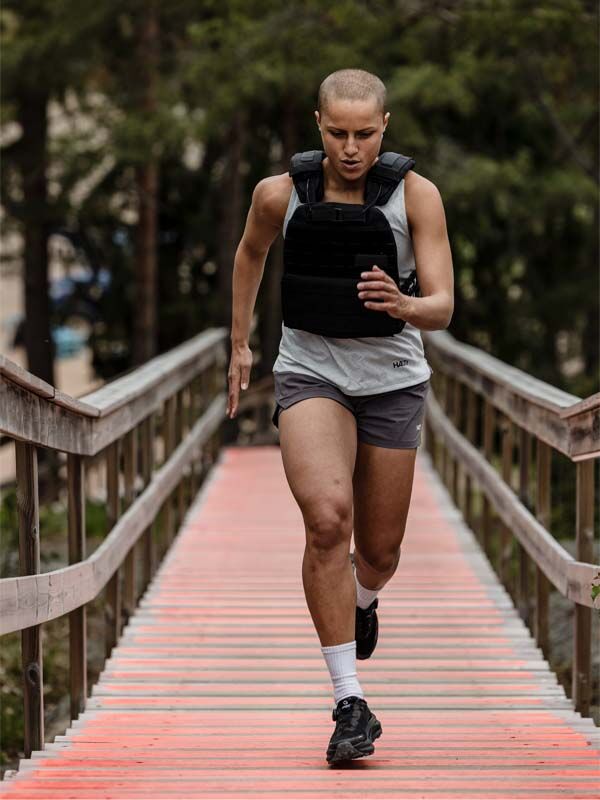 Person med kort hår springer uppför röd trappa i Halti Oulanka T-skjorta Dam, väst med tyngd, shorts och svarta skor.