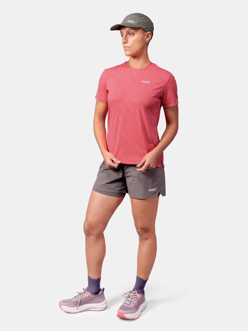 Person i Halti Oulanka T-skjorta Dam, grå shorts, grå mössa, lila strumpor och rosa löparskor.