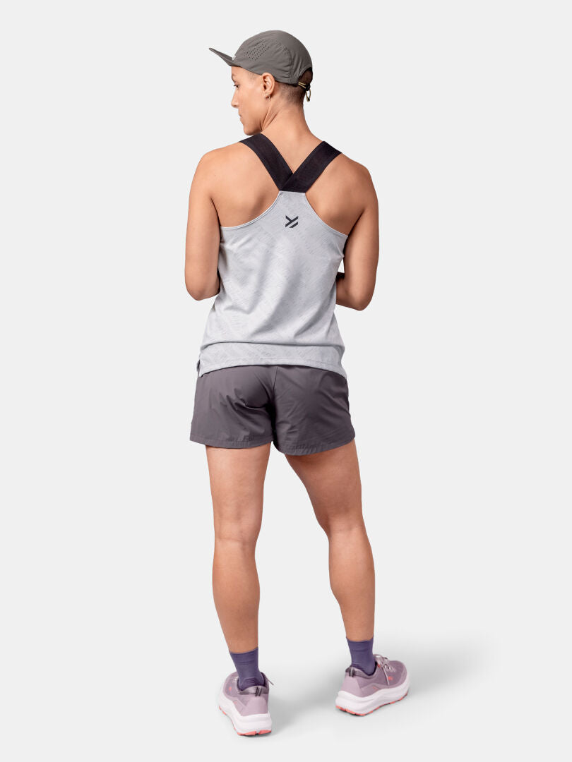 Person iklädd grå Halti Oulanka Träningstopp Dam, grå shorts, sneakers, lila strumpor och keps, sedd bakifrån.