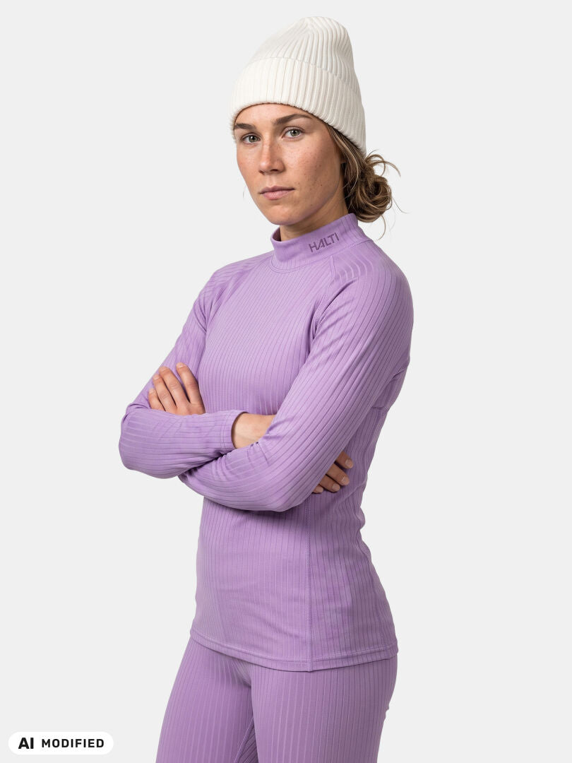 Modellen bär Haltis ”Dual Underställ Set Dam” och en vit mössa, med armarna i kors, samt en matchande lavendelfärgad tröja och byxor.