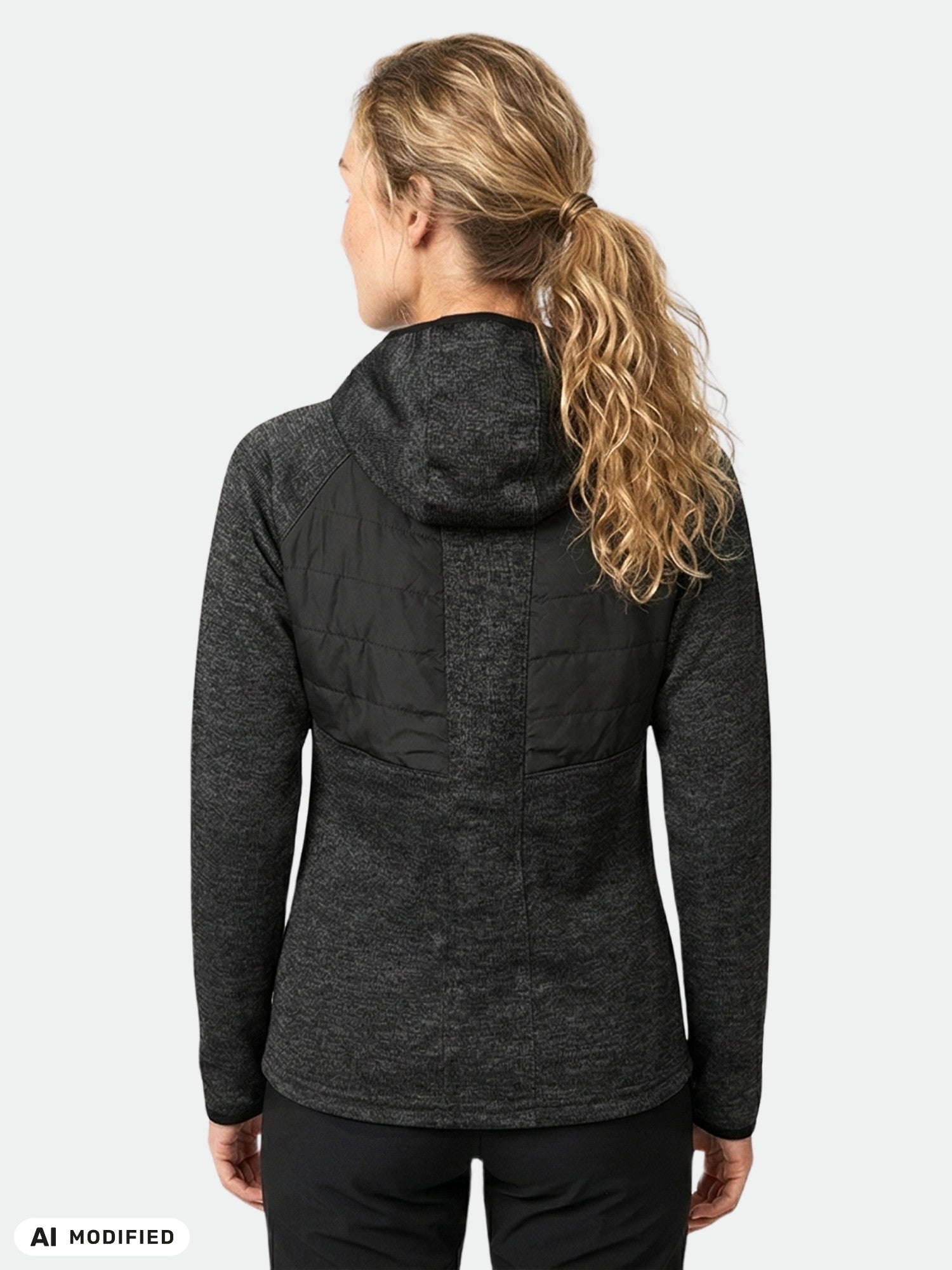 En blond kvinna klädd i en Halti Streams Hybrid Mellanlager Dam-hoodie och svarta byxor står med ryggen mot kameran.