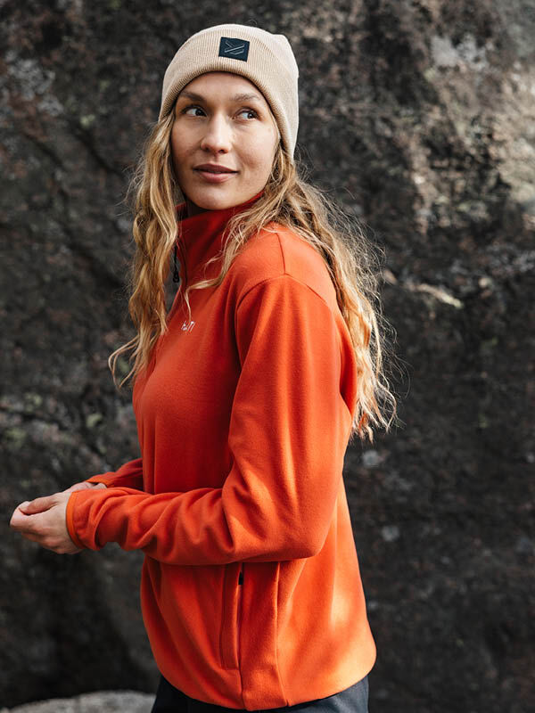 En person i en Halti Rockmoon Fleecejacka Dam står utomhus vid en stor sten och njuter av friluftsliv.