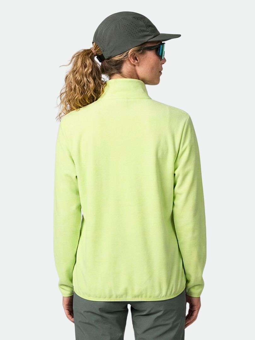 En person som njuter av friluftsliv i ljusgrön Halti Rockmoon Fleecejacka Dam, grå byxor, keps och solglasögon, sedd bakifrån.