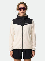 En person är klädd i en gräddvit och svart Halti Rockmoon Fleecehoodie Dam, svarta shorts och stora rosa solglasögon och är vänd framåt.