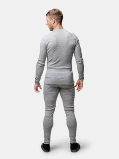 En man bär Halti Hossa II Merino Underställ Set Herr i ljusgrått, med ansiktet vänt bort mot en enfärgad bakgrund.