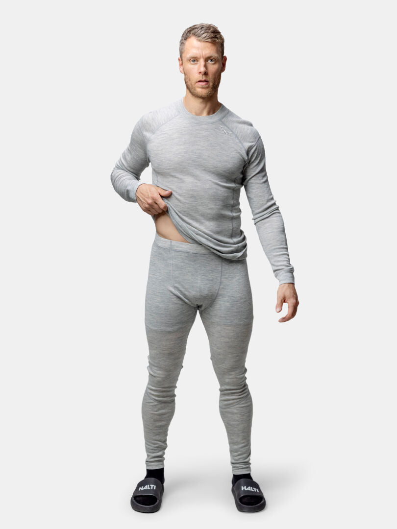 En man bär Halti Hossa II Merino underställ set herr i grå och svarta tofflor, stående mot en enfärgad vit bakgrund.