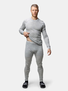En man bär Halti Hossa II Merino underställ set herr i grå och svarta tofflor, stående mot en enfärgad vit bakgrund.