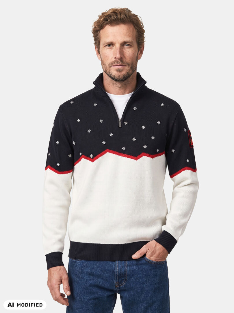 En man klädd i en svartvit Halti Tauko Unisex-tröja med rombmönster och röda kanter, framför en enfärgad bakgrund.