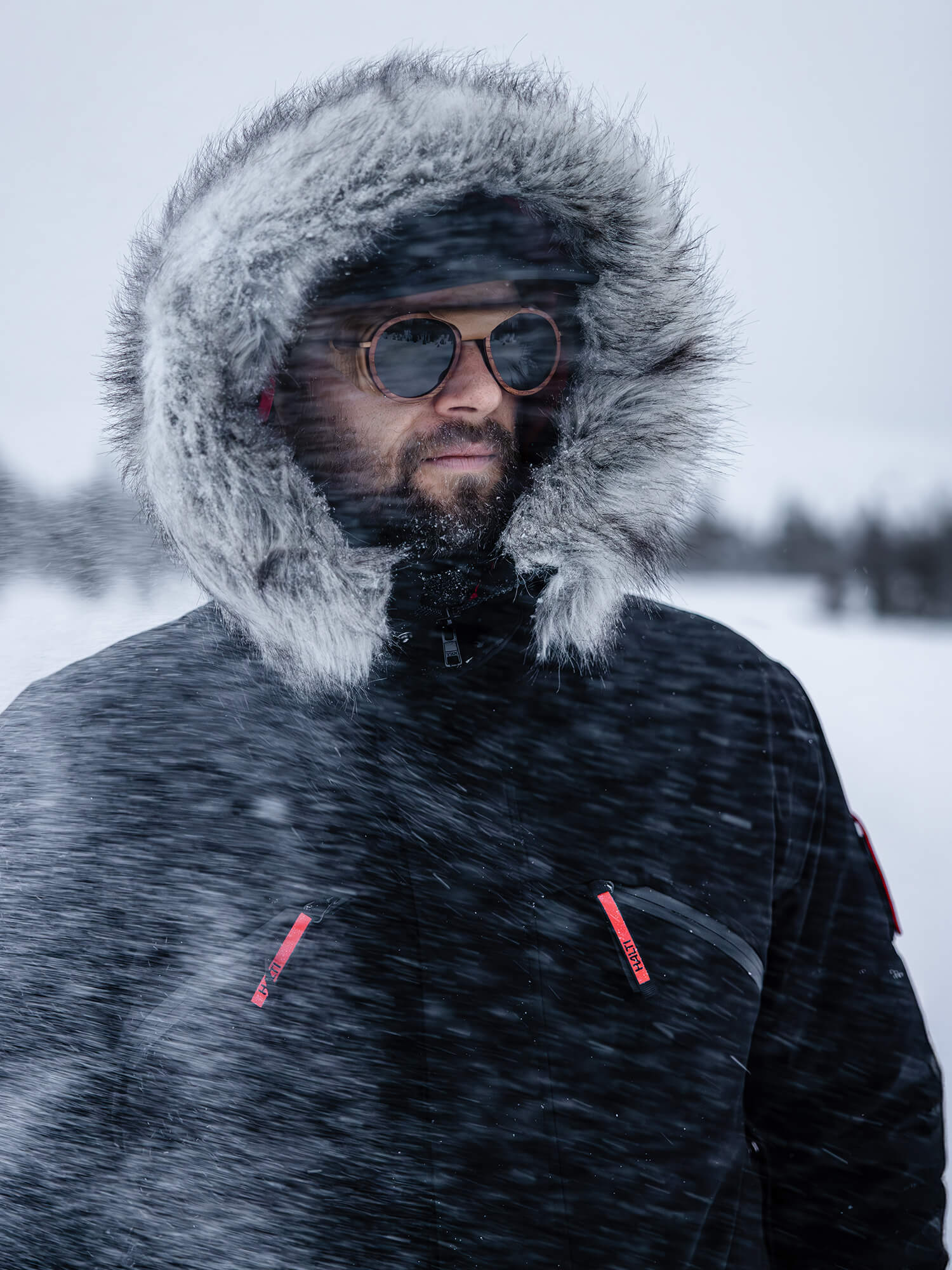 Iförd en Halti Sweden Gåvokort parka, omfamnar en person friluftsliv i snöblandat regn med solglasögon.