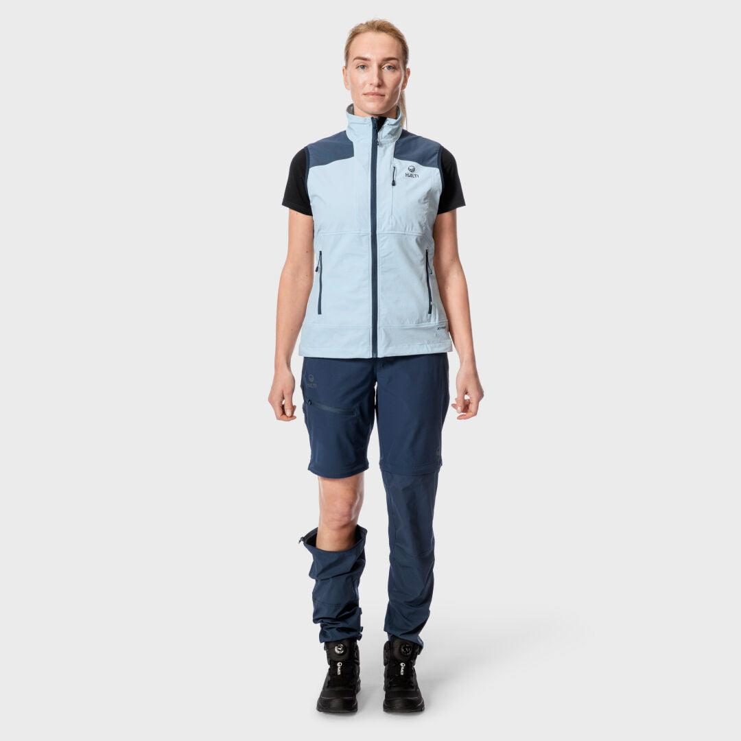 Person som bär en Halti Pallas Dam X-stretch Väst, marinblå byxor med dragkedja och svarta stövlar – perfekt för friluftsliv.